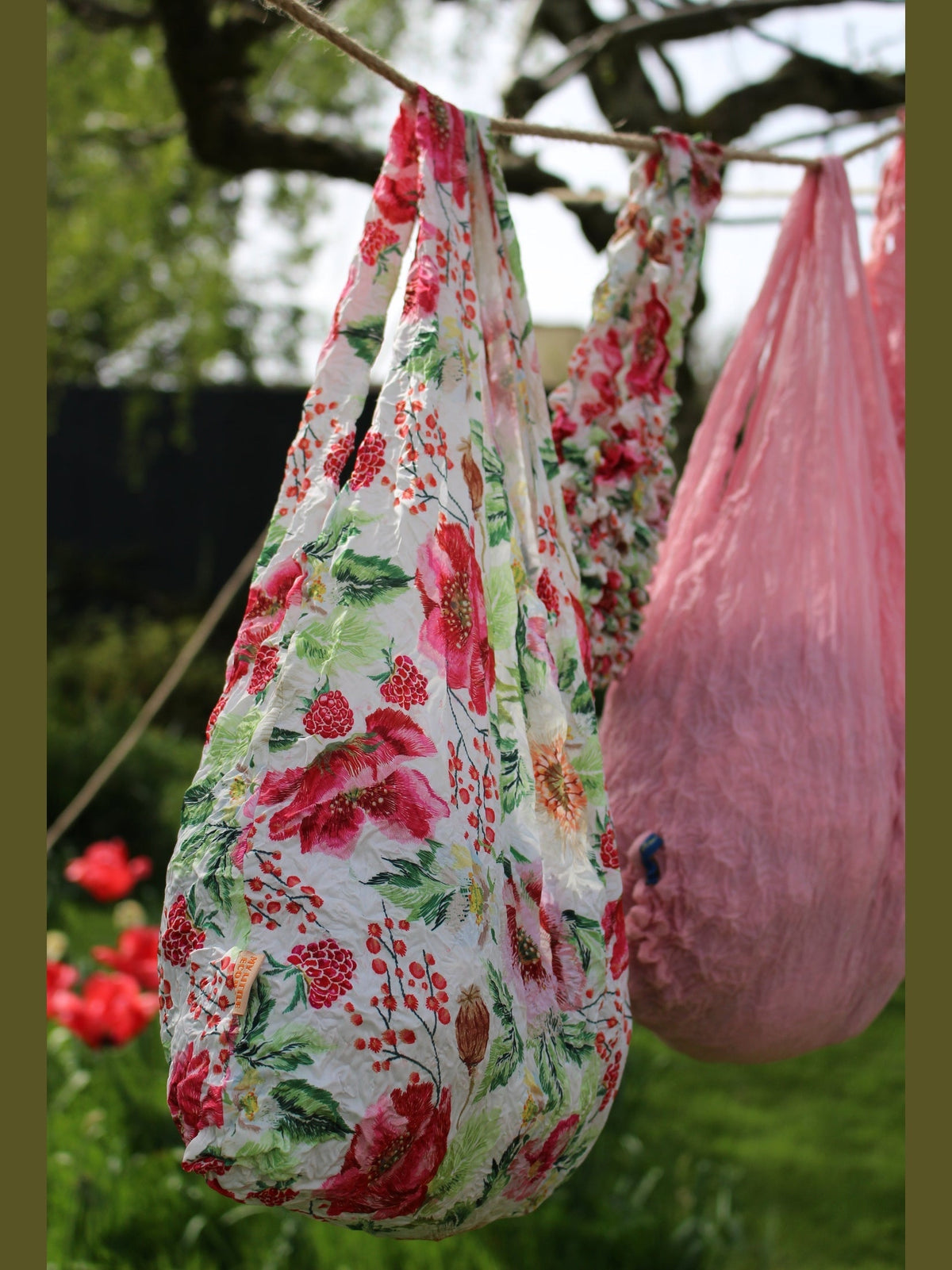 Be Bougie stretchy eco tote bag with a vibrant red berry and floral print hanging outdoors on a clothesline