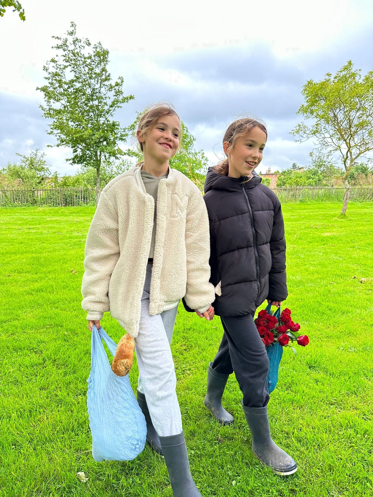 Two girls walking on grass holding Be Bougie French blue sustainable stretchy eco shopper bags with groceries