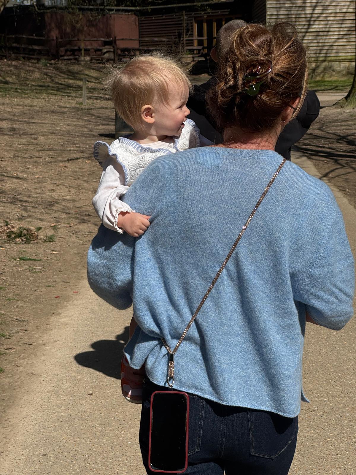Be Bougie gold sparkly cross body phone strap worn by a woman carrying a toddler outdoors