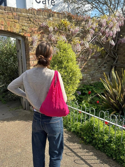 Be Bougie hot pink stretchy sustainable tote bag worn over the shoulder by a woman in a garden setting
